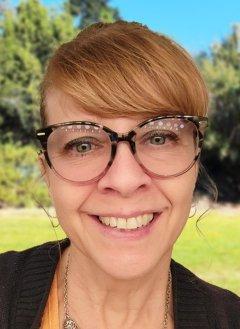 Woman with bangs and hair swept back wearing glasses in front of trees at a college campus.